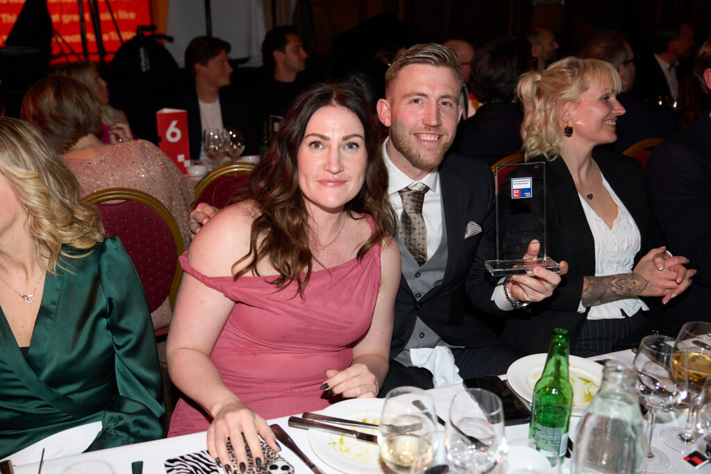 Rebecca Nilsson och Max Malm sitter vid middagsbordet på galan och håller i Great Place to Work-priset med leenden på läpparna.